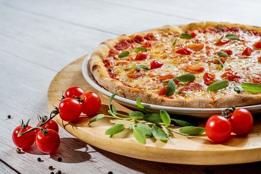 Frisch gebackene Pizza mit Tomaten und Basilikum auf Holzbrett – serviert mit frischen Zutaten