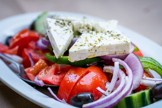 Frischer Salat mit Tomaten, Gurken, Zwiebeln und Feta-Käse auf einem Teller angerichtet